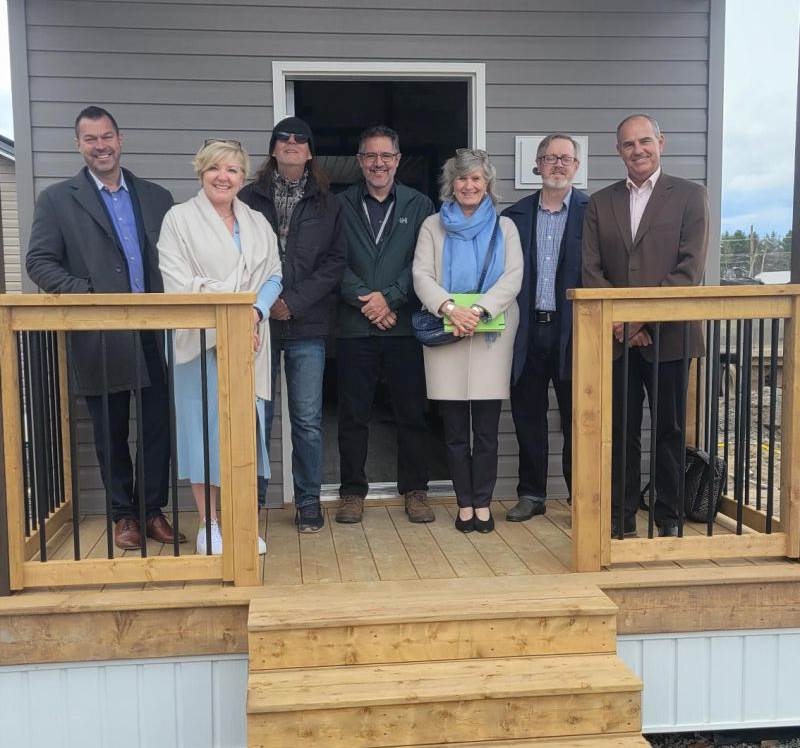 Group of people standing in front of one of the newly built tiny homes in the 12 Neighbours community.