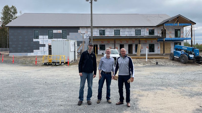 Three men stand in front of a construction site.