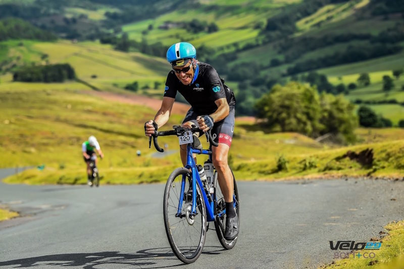 Stephan Gross rides a blue bike along lush, hilly terrain.