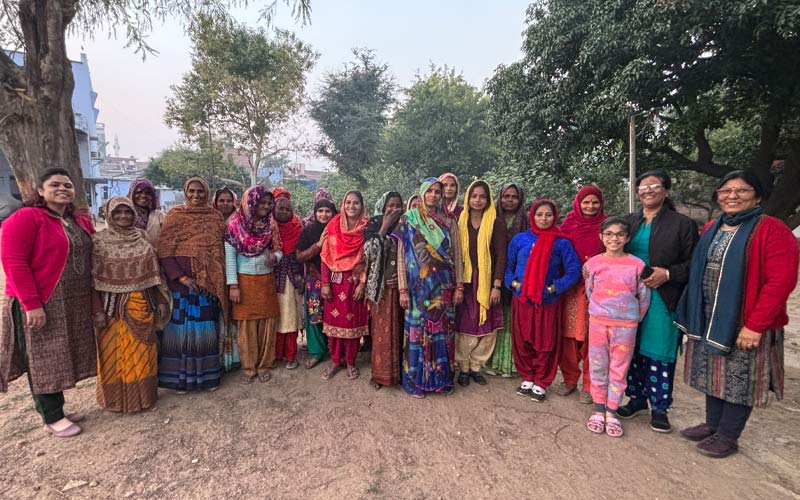 A smiling group of women in colorful attire in a rural setting.