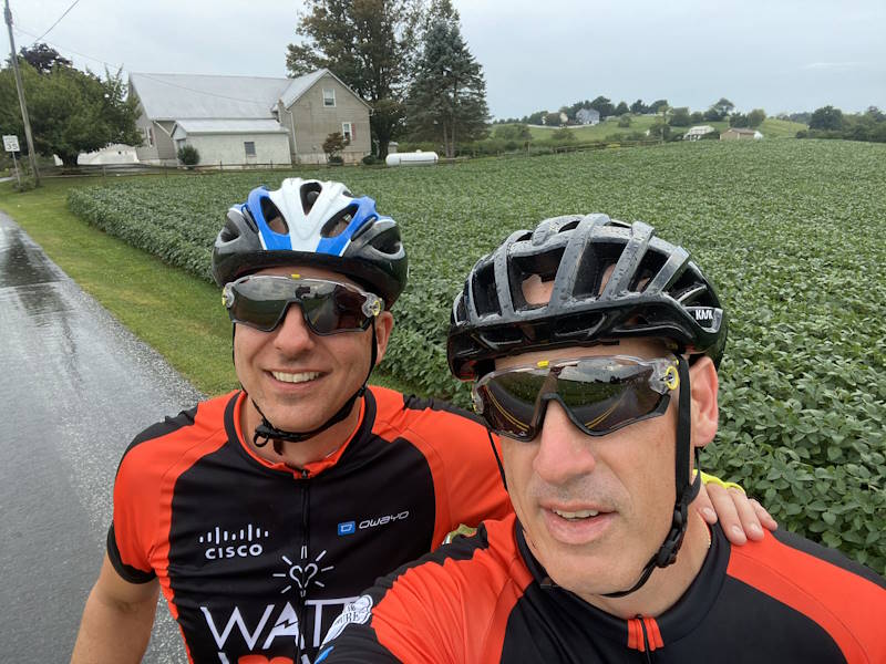 Todd Wilson and Scott pose in their bike gear along a farm.