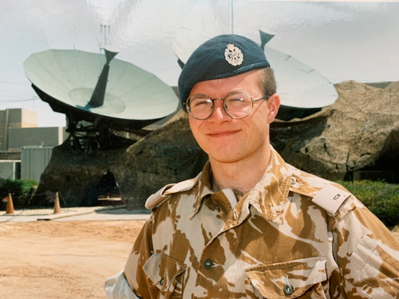 Mat wears Royal Air Force uniform near two satellite dishes.