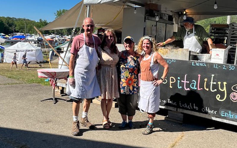 Four volunteers stand arm-in-arm near the hospitality kitchen tent.