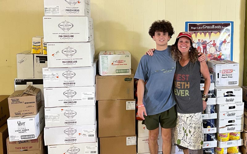 Beth and her son pose for a photo in front of tall stacks of boxes.