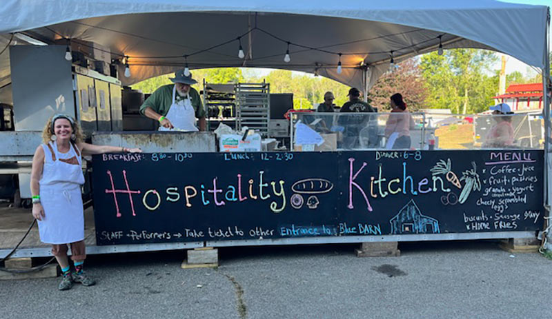 Beth stands by the  hospitality kitchen’s menu board at Shakori Hills.