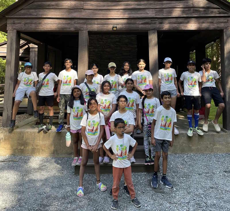 A large group of children pose for a group shot in an outdoor wood shelter.