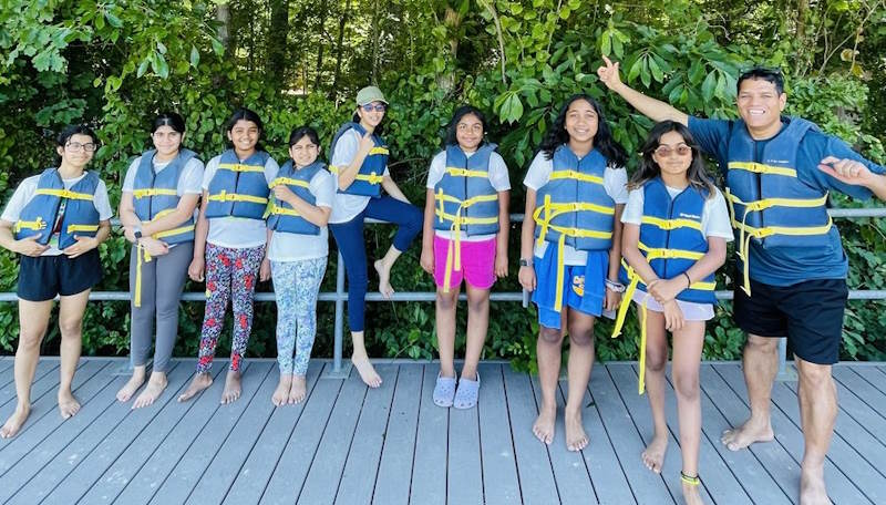 Camp attendees and Vinay wear lifejackets on a deck.