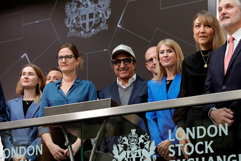 A group of people stand behind a glass barrier with the London Stock Exchange logo on it.