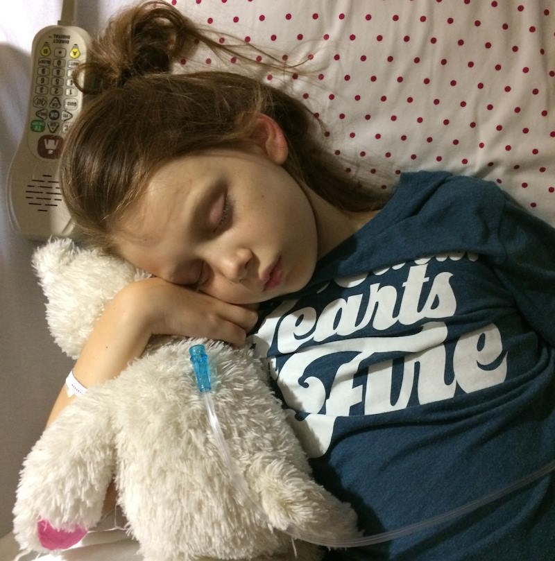 Young girl in a hospital hugging her stuffed bear while sleeping.