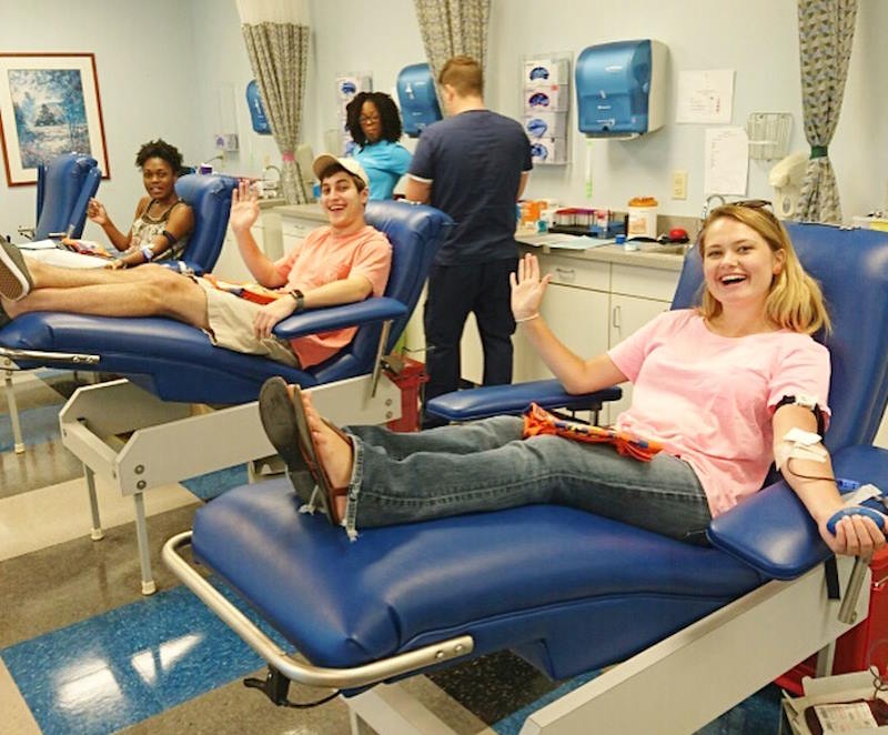 People sitting in blue chairs smiling while giving blood.