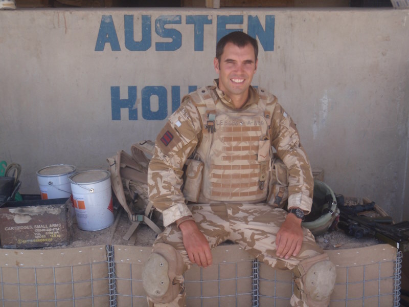 Phil, dressed in brown camouflage military fatigues, sits on supply crates.