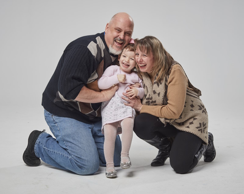 A couple and a young girl kneeling and smiling in a photo studio.