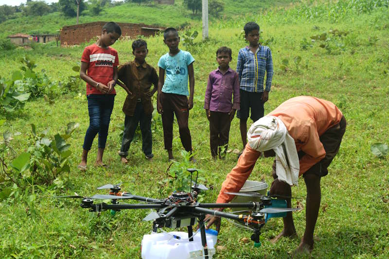 A farmer holds a drone that can monitor and spray crops, while five kids watch.