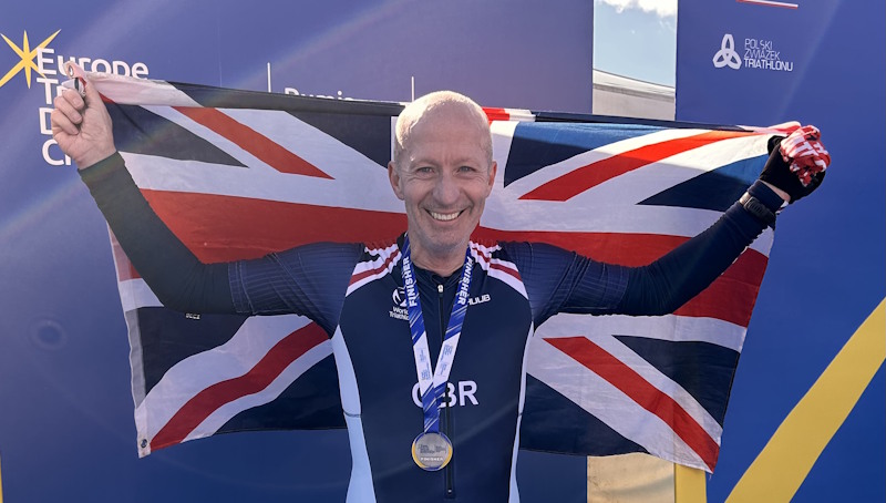 Alastair proudly wears a medal and holds a British flag.