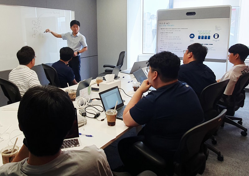 Seven people gathered in an office with a whiteboard.