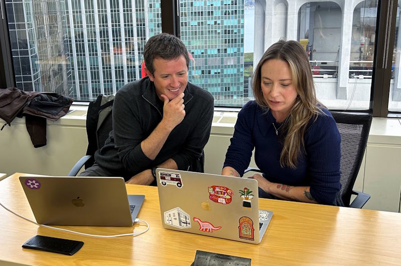 Two people sitting at a table look at a laptop.