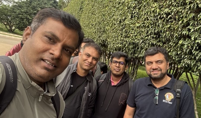 Four people pose together in front of a hedge.