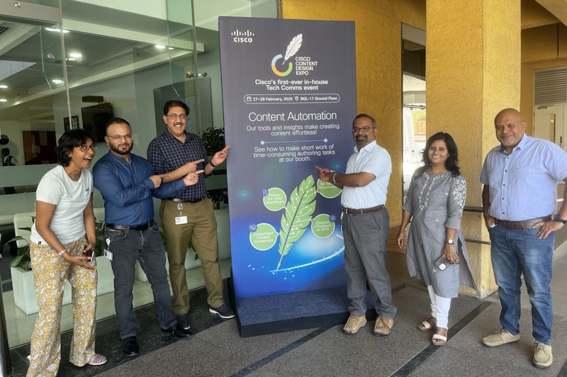Six colleagues smile and point at a tall Cisco banner that says, &ldquo;Content Automation.&rdquo;