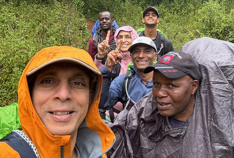 A group  of people wearing raincoats and ponchos smile outdoors for a selfie. 