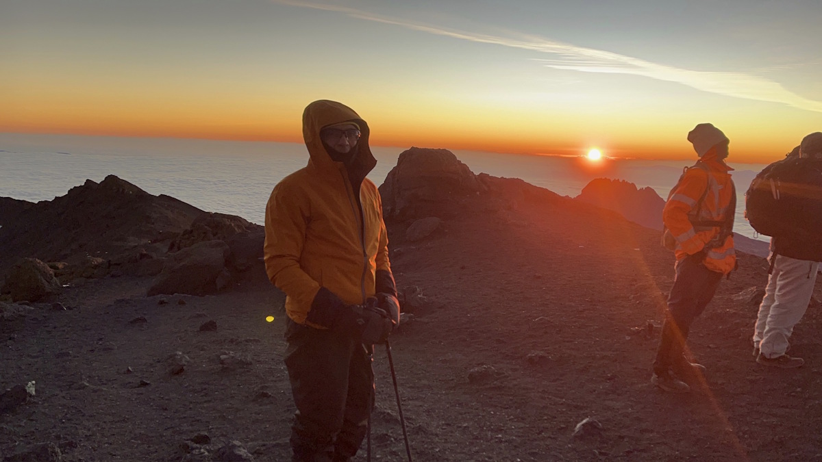 A group of people on a mountain with the sun at the horizon.