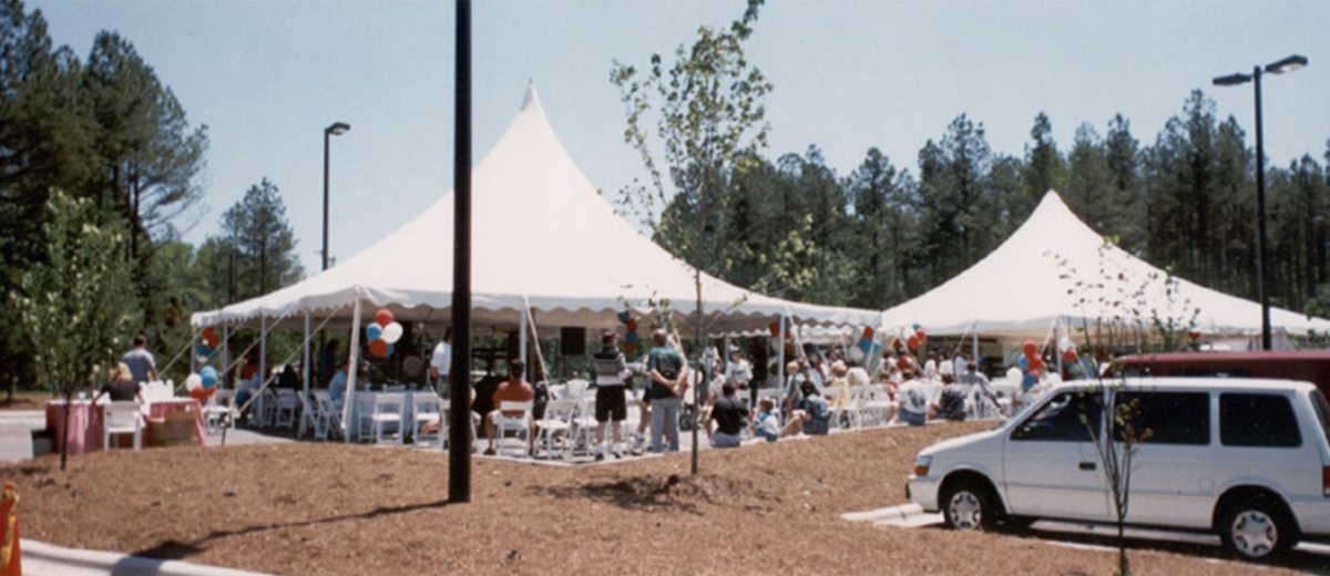 People gather around white event tents with celebratory balloons.