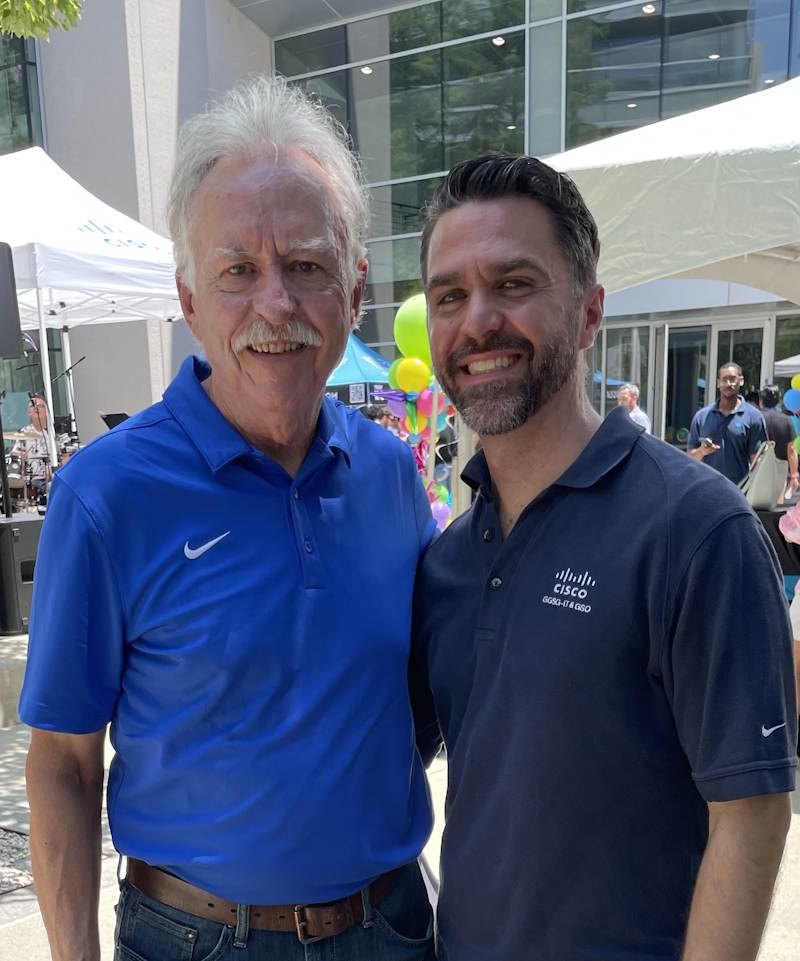 A father and son stand together at an outdoor event, smiling.
