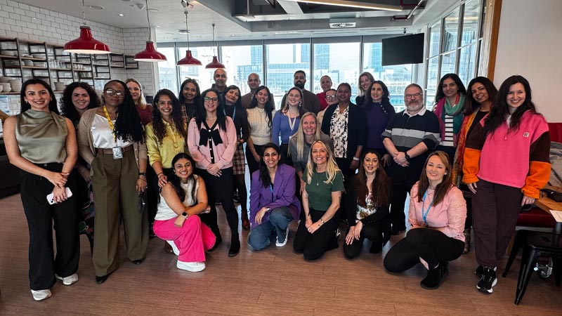 A diverse group of 23 people pose together in a canteen. 