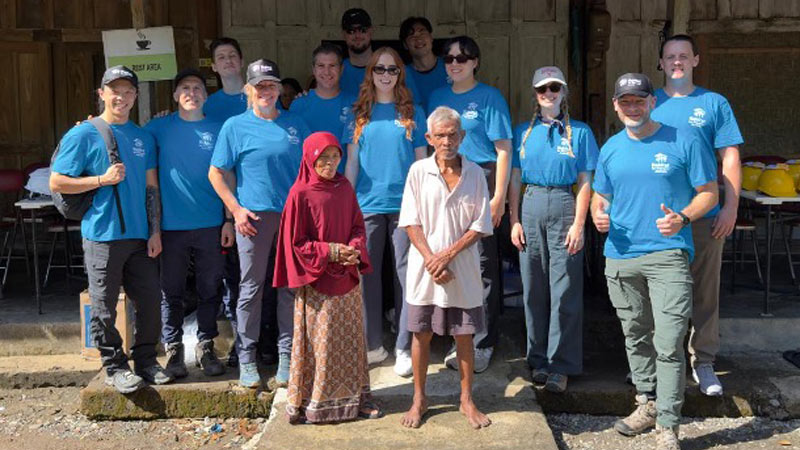 Cisco employees wearing volunteer t-shirts stand with two locals.