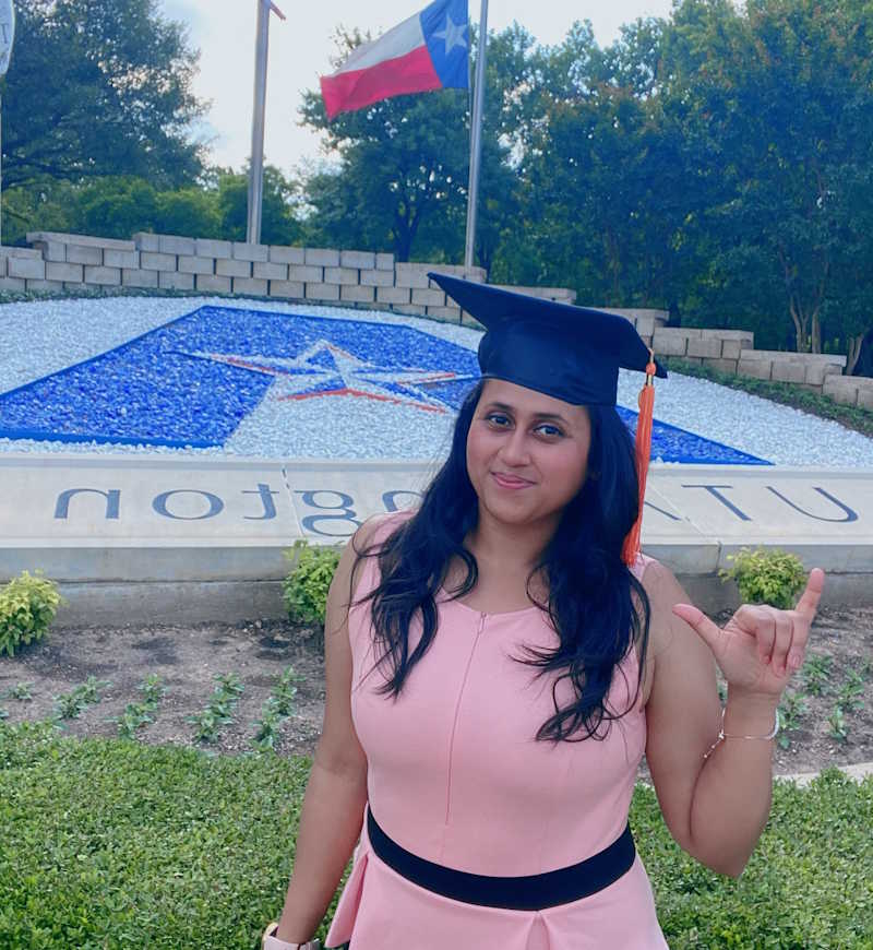 A smiling woman wears a graduation cap.