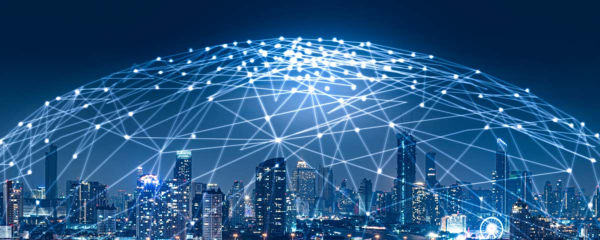 Illustration: City skyline at night with a glowing blue IoT connectivity network overlay.